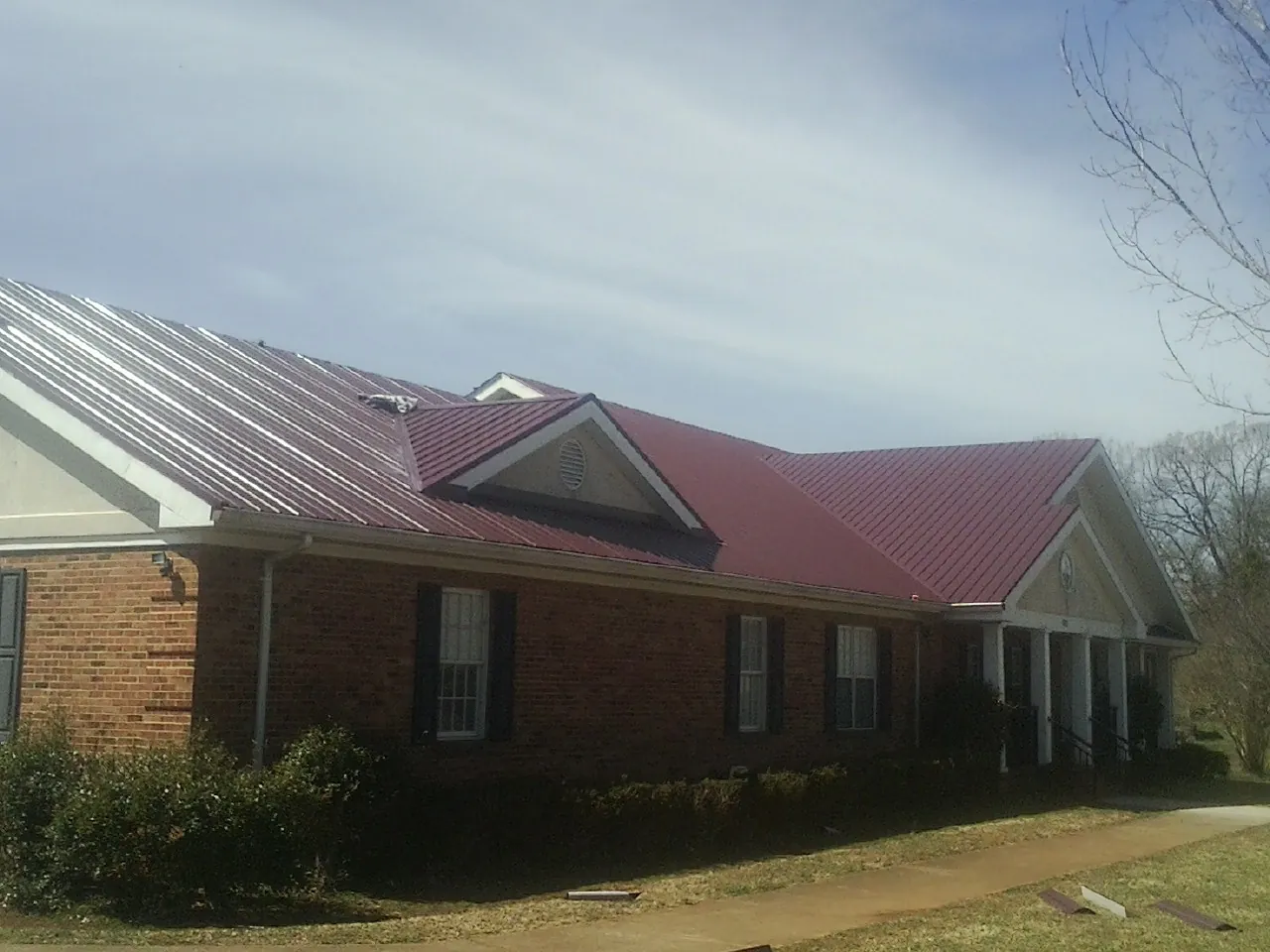 Red metal roof with gabled entries on a long brick building, from a Hail Damage Roof Repair job in Yakima
