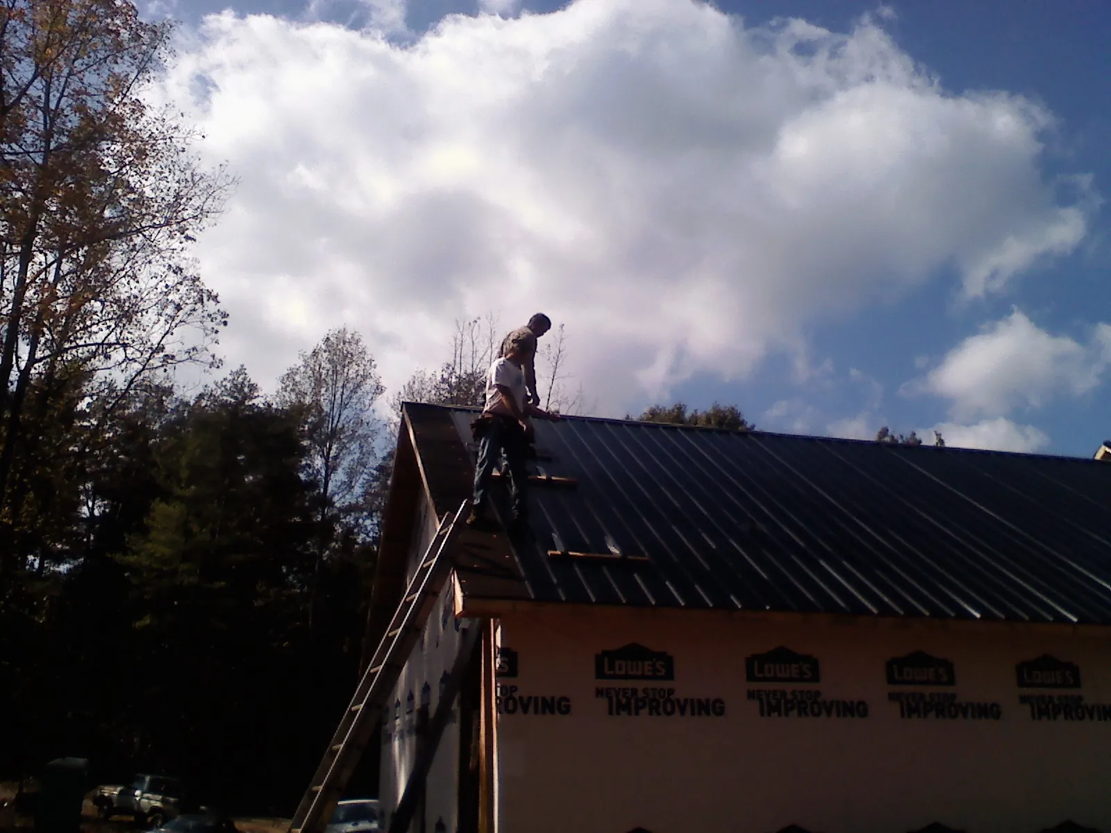 Roofer fastening dark metal panels high against a cloudy sky, from a Roof Inspection job in Yakima
