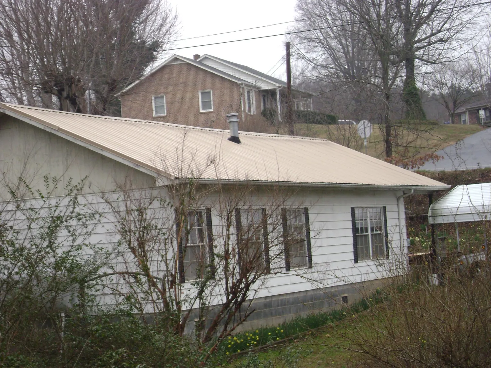 Tan metal roof on a white sided house set into a hillside — Commercial Roofing by Roofing Brothers in Yakima